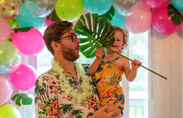 Young father holding little girl at a tropical theme birthday party at home
