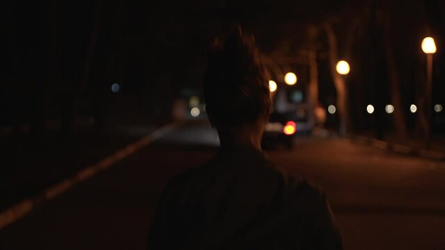 Girl in blue jeans shirt running down the street at night. Meida. Rear view of a young woman running in the streer late in the evening along the street lamps.