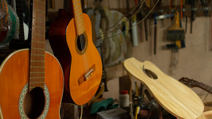 Two hanging wooden guitars and guitar parts on the carpentry table in a workshop