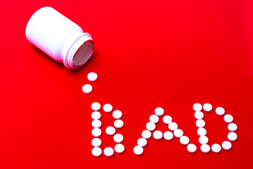 The word Bad spelled out in white circular pills with a white pill plastic bottle on a red background