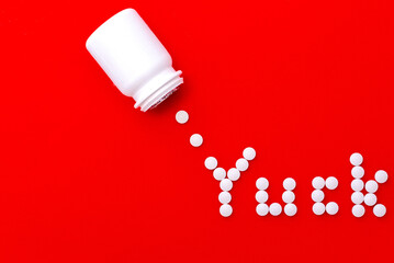 The word Yuck spelled out in white circular pills with a white pill plastic bottle on a red background