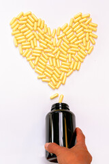 Yellow powder capsules pouring out into a heart shape from an amber plastic pill bottle  on a white background.