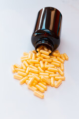 Yellow powder capsules pouring out of an amber plastic pill bottle  on a white background.