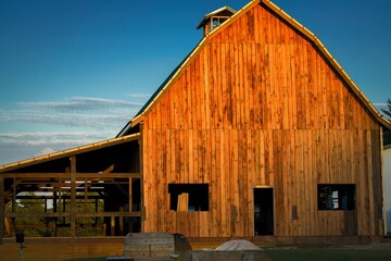 This image shows a rustic wooden barn and stables with a blue sky background in a remote location.