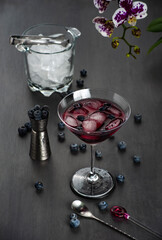 Cocktail in a glass, blueberry fruit, orchid flower, ice bucket,  dark gray background. Select focus