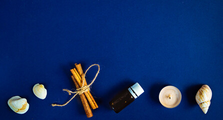 Obraz na płótnie Canvas Dark blue background. Essential oil bottle , scented candle, sea shells, cinnamon sticks. Aroma therapy concept. Spa procedures. Witchcraft tools. Esoteric.