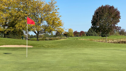 Obraz premium early autumn golf course green red flag leaves changing treetops 