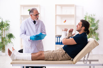 Obraz premium Young injured man visiting old doctor traumatologist