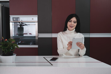Young relaxing women playing digital tablet in kitchen