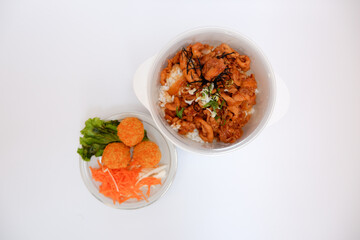 Japanese chicken rice, as known as Tori Don, is a chicken fillet cooked with japanese sauce placed on rice in a bowl. Tori don and three fish balls with vegetables beside it on a white background.