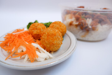 Three fried fish balls on a white background. Side view of fish balls that placed on a white plate with vegetables topping beside it and a bowl of tori don behind it.