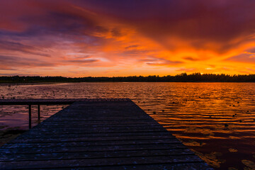 Naklejka na ściany i meble Incredible sunset landscape with a wooden pier on a stunning forest lake