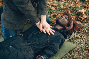 Guy help a woman. African girl is lying unconscious. Providing first aid in the park.