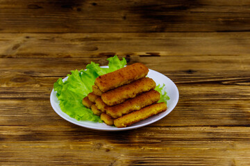 Fried fish fingers on a plate with lettuce on wooden table