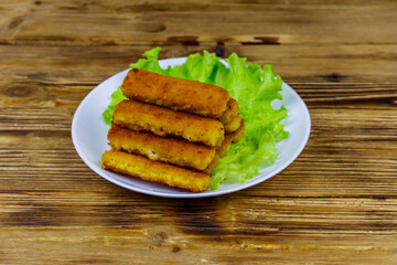 Fried fish fingers on a plate with lettuce on wooden table