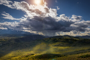 Mysterious mountain landscape with storm clouds hills and sun rays. Beautiful sky. Green grass on...