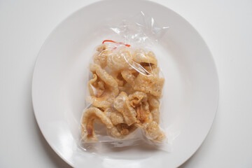 pork snack, pork rind, pork scratching in plastic bag on white plate and white background