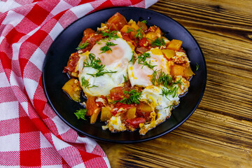 Homemade breakfast shakshuka - fried eggs, onion, bell pepper, tomatoes and dill on rustic wooden table. Jewish cuisine