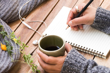hand of woman holding hot tea with writing notebook for business work and knitting wool scarf of lifestyle in winter season decoration on table 