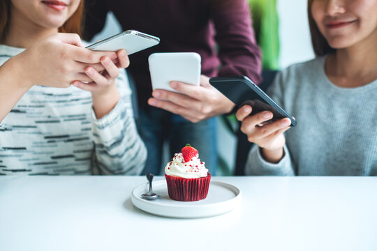People using mobile phone to take a photo of a cupcake before eat in cafe