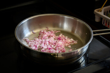 Chopped small onion getting cooked with oil on a stainless steel frying pan