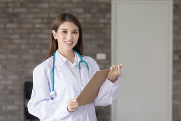 Young beautiful Asian woman doctor working at hospital. She wear a white robe and stethoscope and hold a clipboard in her hands.