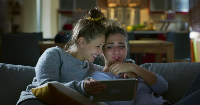Authentic shot of young happy just married homosexual female gay couple in love enjoying time together while using tablet for family entertainment on sofa in living room before going sleep at home.