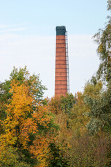 old red brick factory chimney behind the beautiful colorful autumn trees