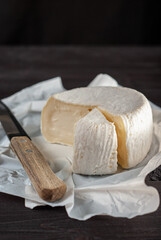 Creamy Camembert cheese on natural dark wooden background, just unpacked from white paper with one...