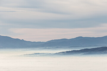 Fototapeta na wymiar Fog filling a valley in Umbria (Italy) at dawn, with layers of mountains and hills