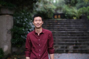 medium shot of one young Asian man looking at camera and smile, in natural park