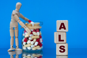 ALS - word on a wooden block on a blue background with pills and a wooden man