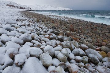 Beach with round stones on a cloudy February day. Coast of the Arctic Ocean in the vicinity of the village of Teriberka. Murmansk region, Russia