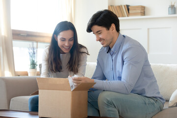 Wow! Excited curious millennial spouses husband and wife opening unpacking awaited parcel with interest and pleasure, glad happy young family receiving order or delivery from internet shop by mail