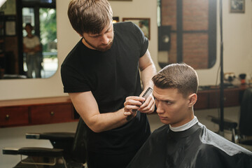 Presision work from hairdresser combing young man's hair in a barber shop