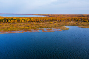 Aerial photo of a surface of the lake surrounded by colorful forest in autumn.