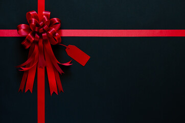 Red ribbon with bow and price tag on black background. Black friday concept.