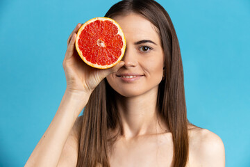 Natural organic raw fresh food concept. Smiling, attractive girl holding half of grapefruit on blue isolated background