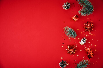 Christmas composition with copy space. Fir tree branches with xmas decoration and festive confetti on a red background, top view
