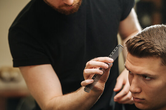 Close up image hairdresser combing young man's hair in a barber shop