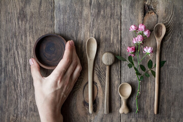 Top view few wooden spoons and rose branch on wooden table, eco-friendly concept of cutlery, handmade tableware production