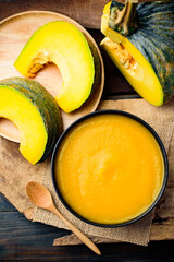 Pumpkin soup in a bowl with spoon and fresh pumpkins on wooden table