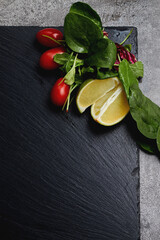 Lime, lettuce, greens and red cherry tomatoes lie on a dark stone slate background, space for text, restaurant menu
