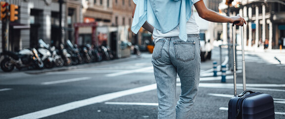 Young traveling woman with suitcase on a sunny city street. Traveler on vacation. Waiting for taxi