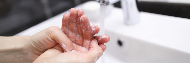 Fototapeta premium Close-up of person carefully washing hands with soap under water. Prevention infection spread. Clean white modern faucet in bathroom. Silver crane. Personal hygiene concept