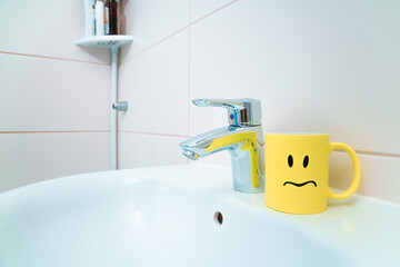 chromed metal faucet for hot and cold water,  cup with sad face for toothbrushes  in a modern...