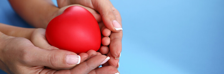 Close-up of mother and child holding red heart in hands on blue background. Motherhood and protection. Copy space in right side. Family relationship and charity and adoption concept