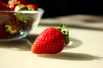 Fresh ripe delicious strawberries in a glass plate on the table. Breast of red strawberries on a plate close-up. One strawberry is lying next to it. Copying space for text