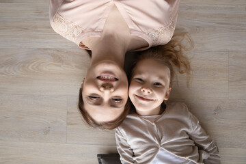 Top view headshot portrait happy little girl with mother lying on warm wooden floor, overjoyed...