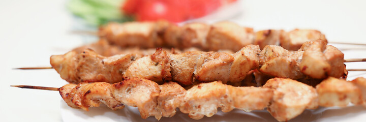 Close-up of delicious grilled chicken pieces on bamboo skewers on white plate. Aromatic meat for dinner or lunch. Home barbeque. Tasty meal and healthy food concept
